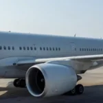 a large twin-engine widebody commercial aircraft parked on an airport apron, viewed from a low angle emphasising the wing leading edge and engine nacelle, clean morning daylight