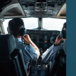 nside a modern pressurized business jet cockpit at high altitude, two pilots seen from behind in natural working posture, one quick-donning oxygen mask